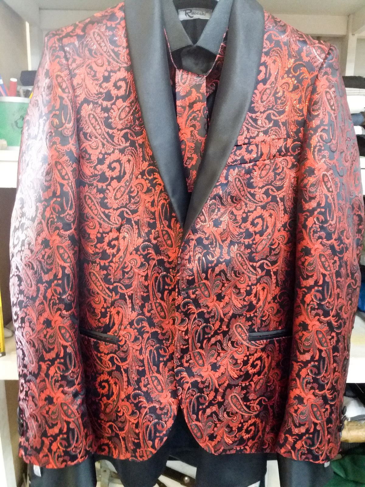 Una giacca da smoking rossa e nera e una cravatta sono appese a una gruccia.