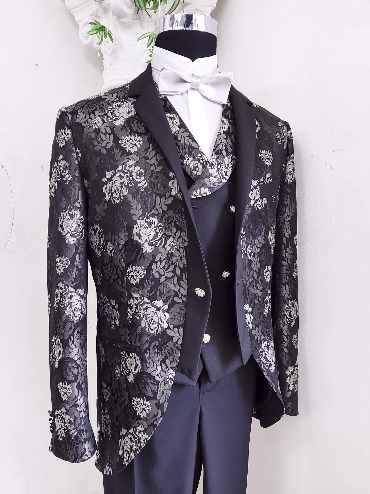 Un uomo indossa un abito nero con fiori argentati sopra