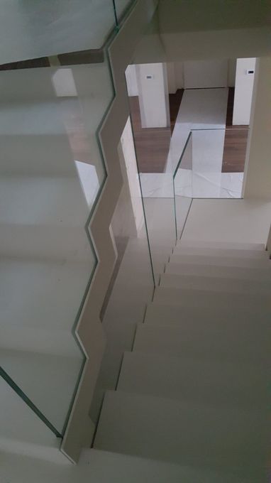 Vano scale in vetro con gradini e ringhiere bianche all'interno di un edificio.