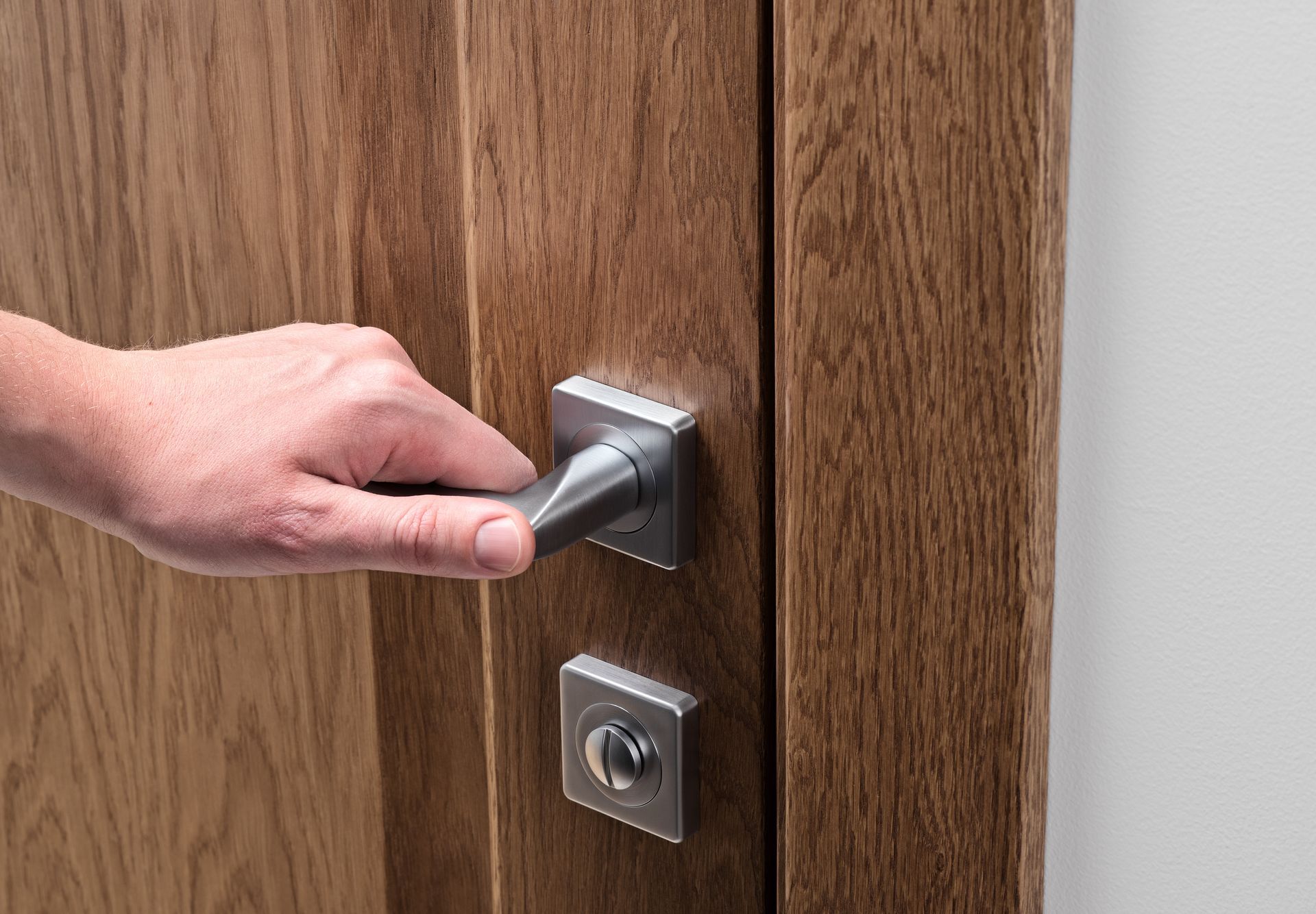 Mano che gira una maniglia d'argento su una porta di legno con una serratura sottostante.
