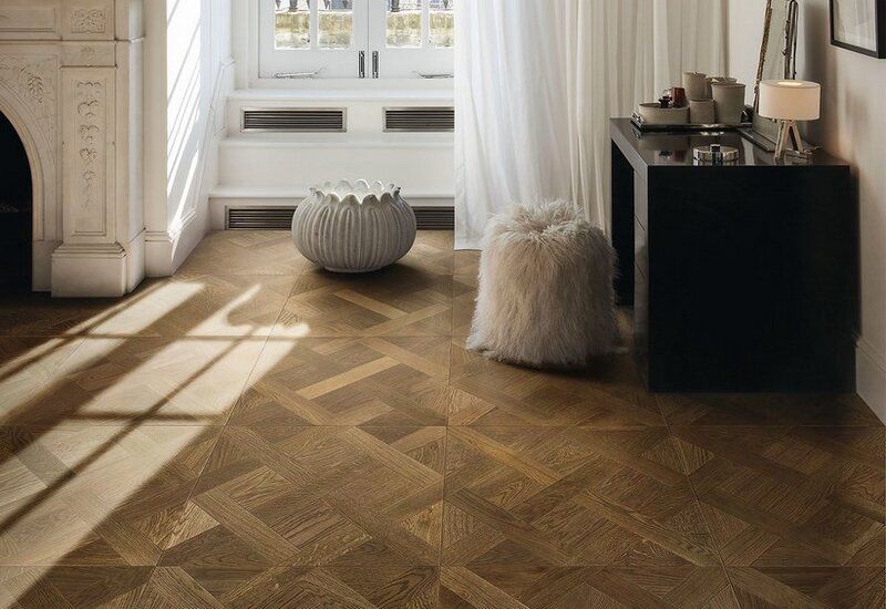 Soggiorno luminoso con pavimento in legno a spina di pesce, tende bianche e due piccoli pouf decorativi.