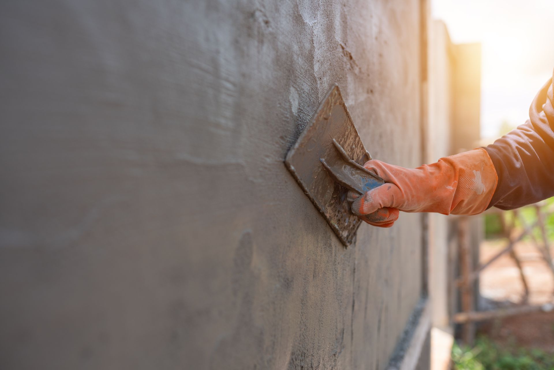 Un operaio liscia il cemento fresco su un muro all'aperto con una cazzuola.