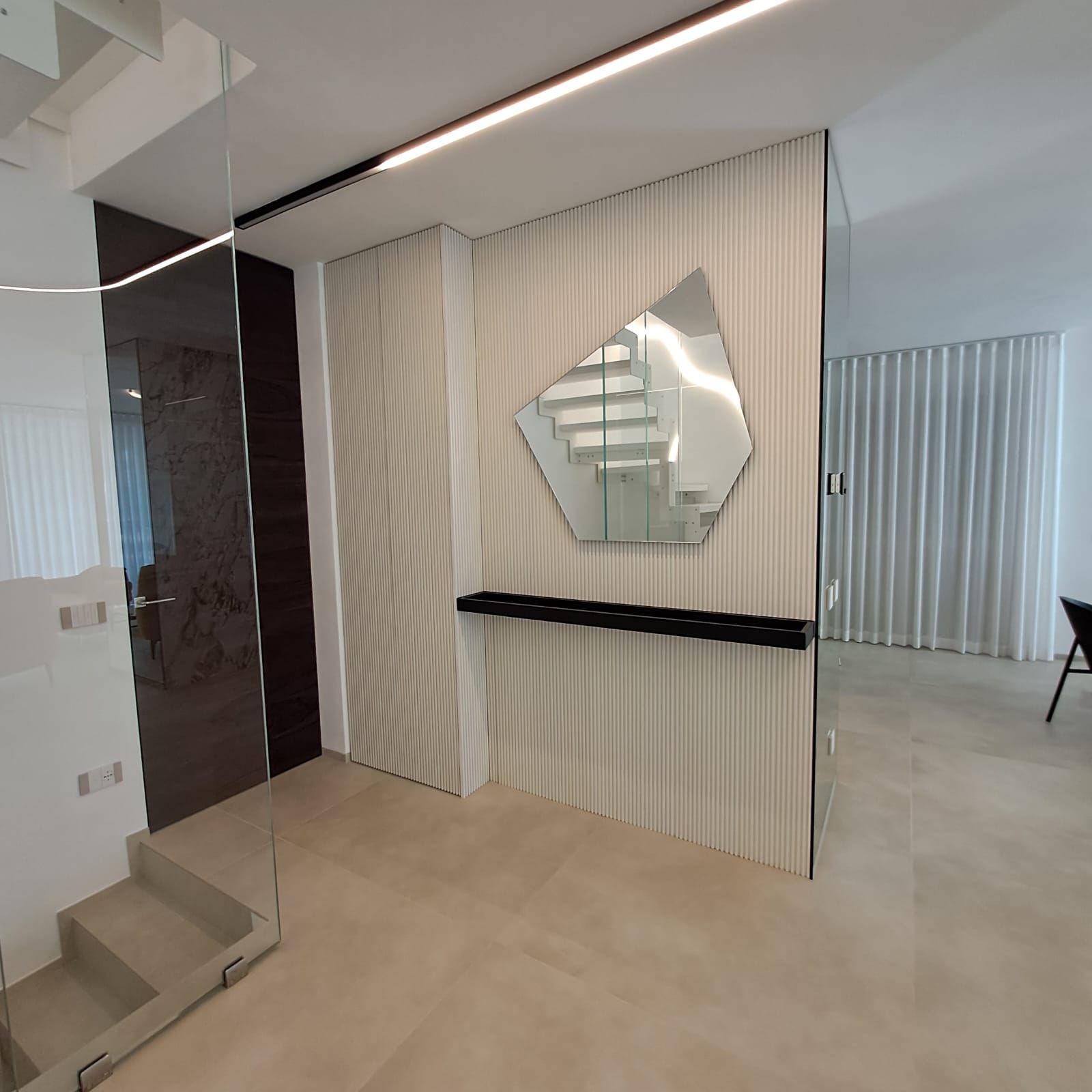 Interni moderni della hall con scala, specchio a parete, pavimento beige e parete decorativa a righe verticali.