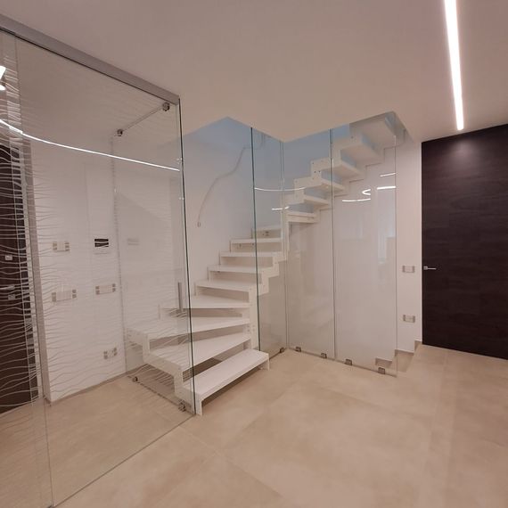 Interno moderno con scala bianca, pareti in vetro e porta in legno scuro in una stanza minimalista