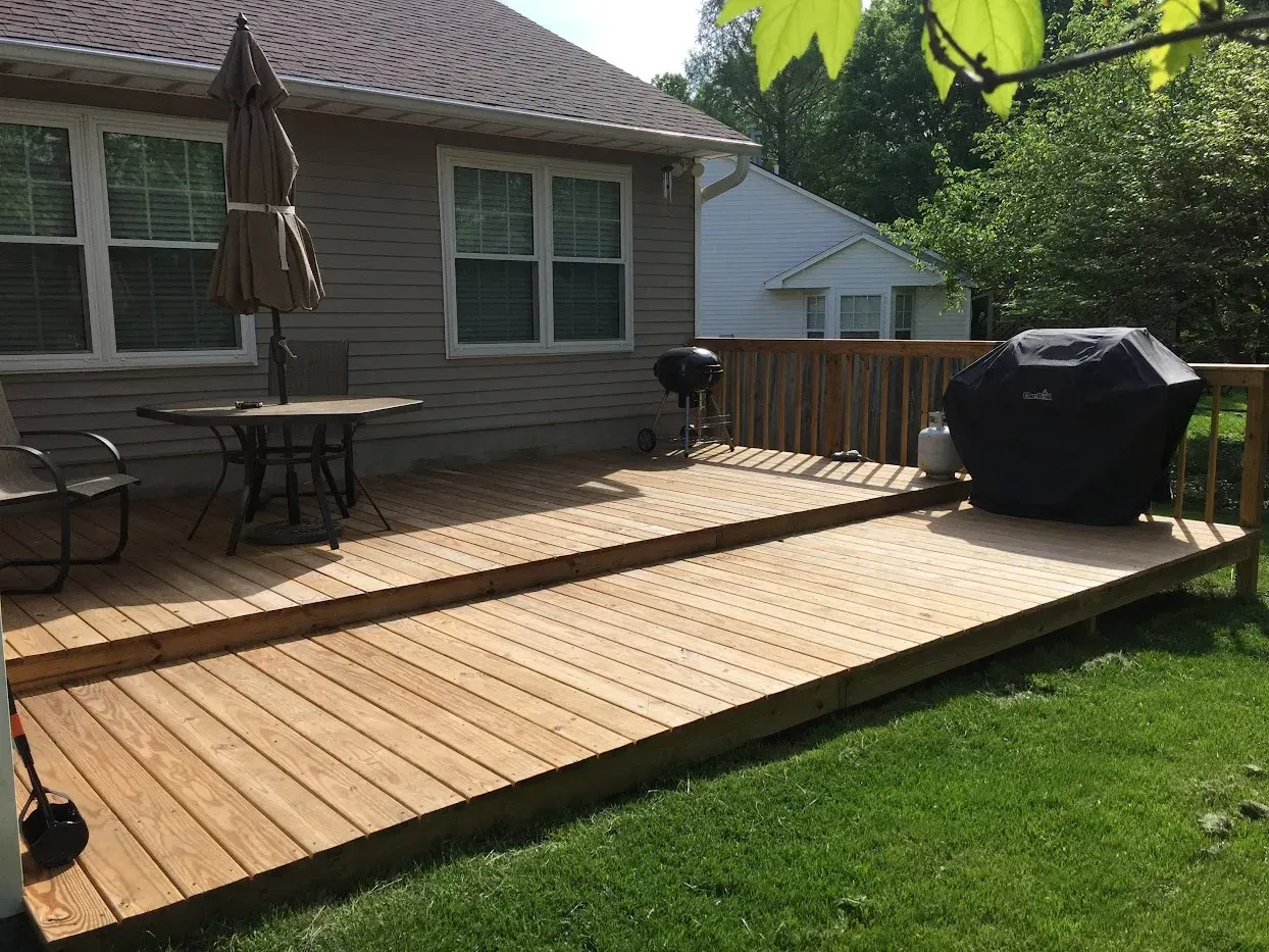 Wooden deck with a grill, table, and chairs in a backyard.