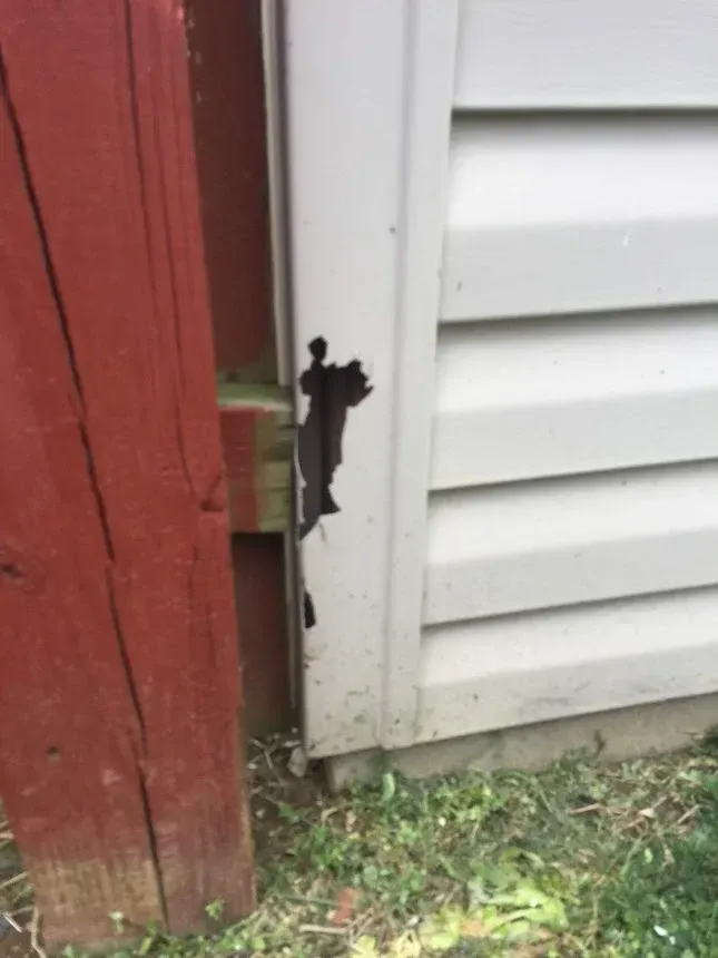 Damage to off-white siding next to a red wooden post. Black scorch marks and missing siding.