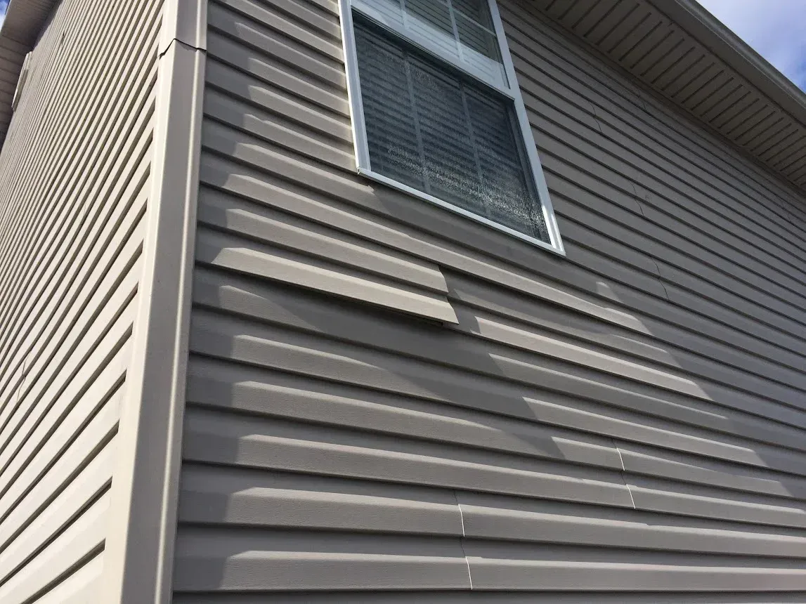 Gray vinyl siding on a house with a window and an open vent.