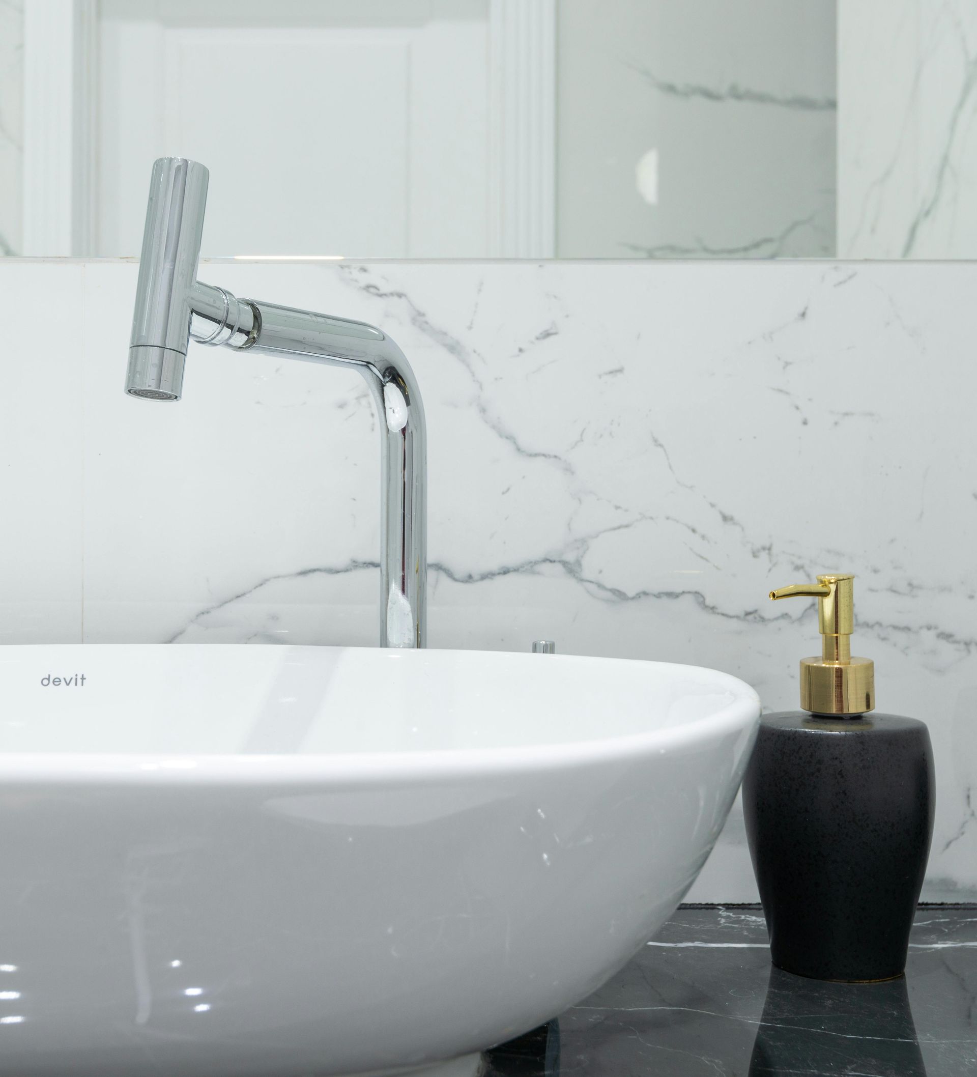 White sink with chrome faucet and black soap dispenser in bathroom.