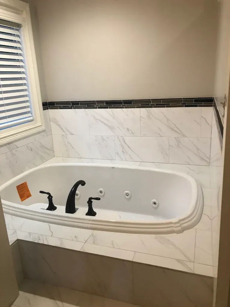 Bathroom with built-in jacuzzi tub. White marble tiles and black accents. Dark fixtures.