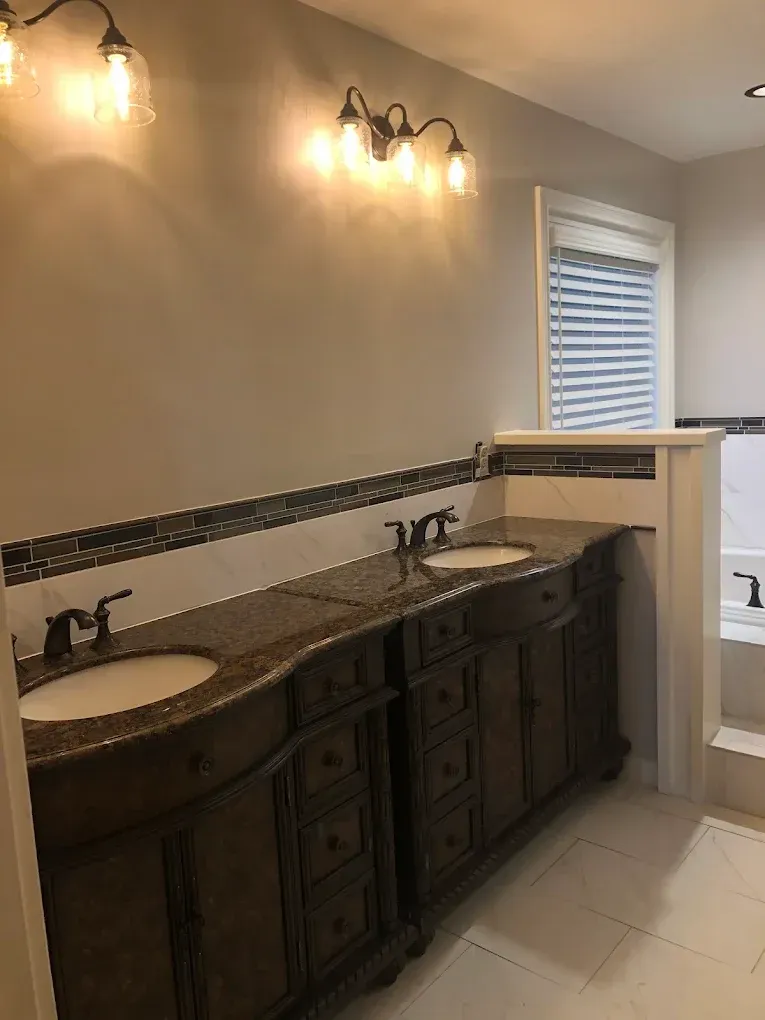Bathroom with two dark wood vanities, granite countertops, and three-bulb light fixtures.