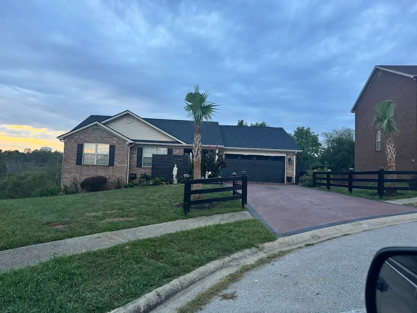 Brick house with a black gate and driveway, cloudy sky.