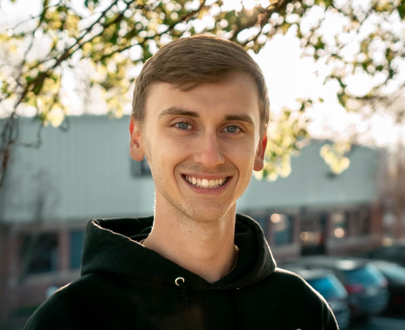 A young man wearing a black hoodie is smiling for the camera.