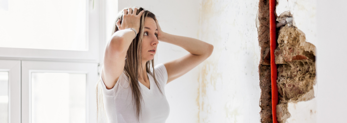 Woman looks at demolished wall upset because of her expensive plumbing repair