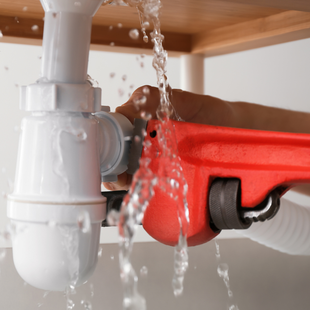 Plumber fixing a leaky elbow joint with a red pipe wrench
