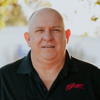 A bald man is wearing a black shirt with the word george embroidered on it.