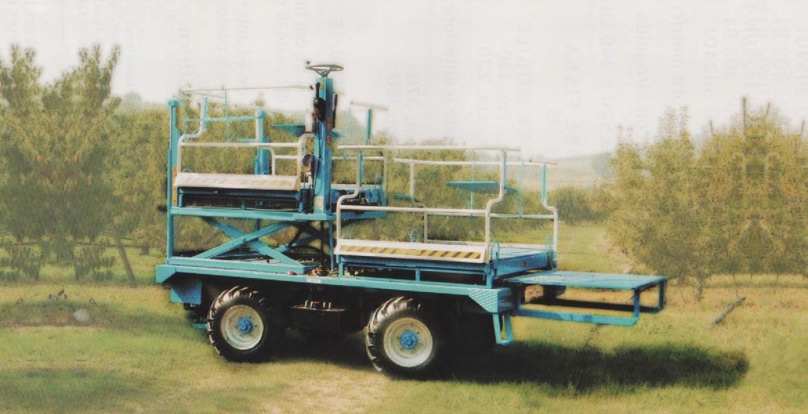 Macchina raccoglitrice blu per frutteti in un campo con alberi.