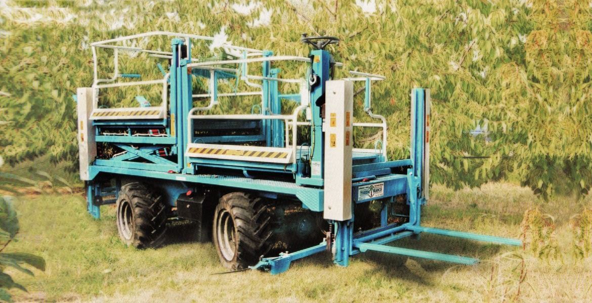 Macchina agricola blu con pneumatici di grandi dimensioni e un carrello elevatore, all'aperto nell'erba alta.