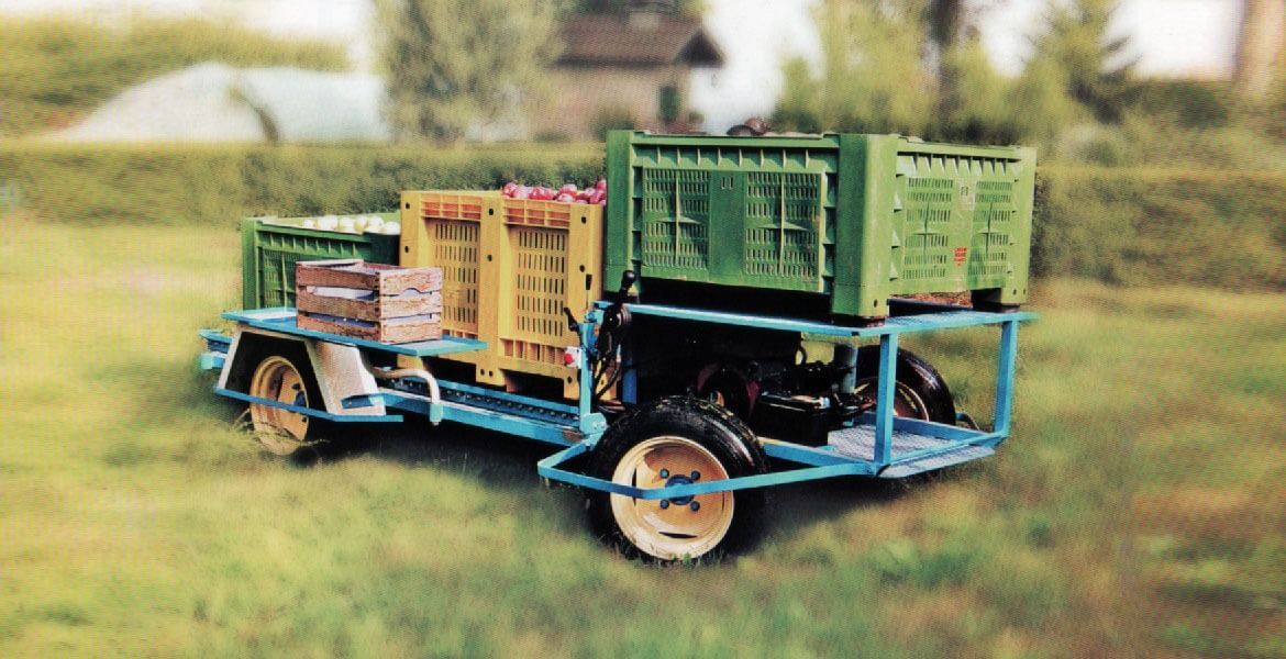 Un piccolo veicolo agricolo blu con casse di prodotti accatastate su un campo erboso.