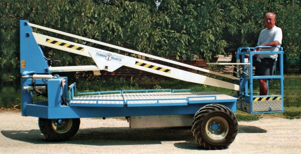 Cestello elevatore blu con piattaforma elevata. Un uomo è in piedi sulla piattaforma. All'aperto, di giorno.