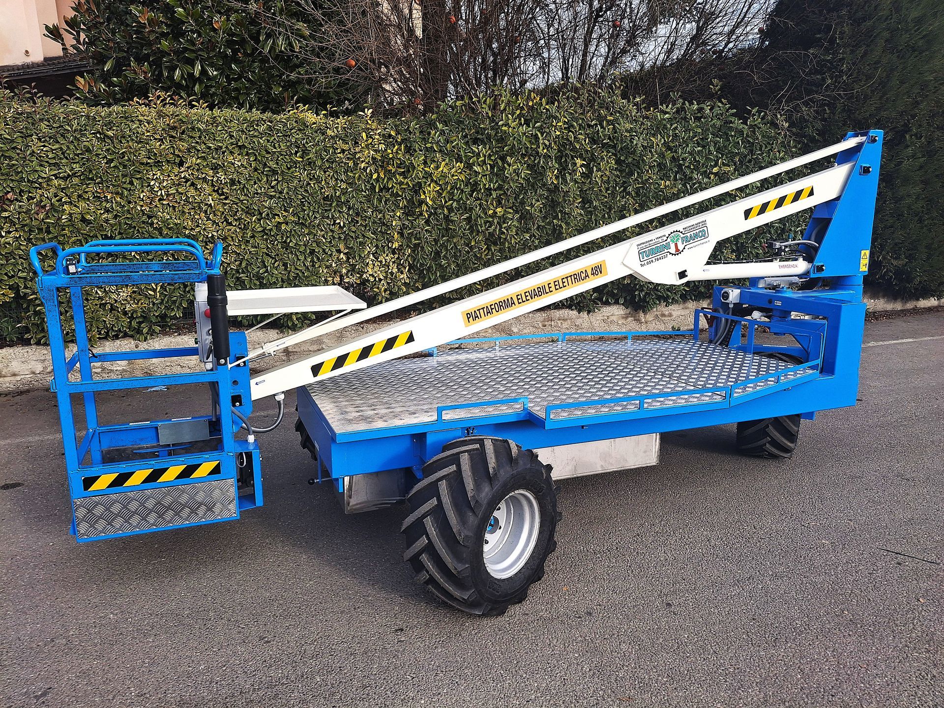 Piattaforma aerea industriale blu e bianca sul cassone di un camion, parcheggiata vicino a un edificio in mattoni.
