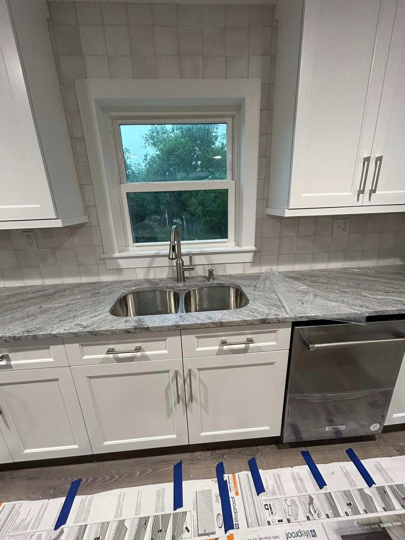 A kitchen with white cabinets , granite counter tops , a sink and a window.