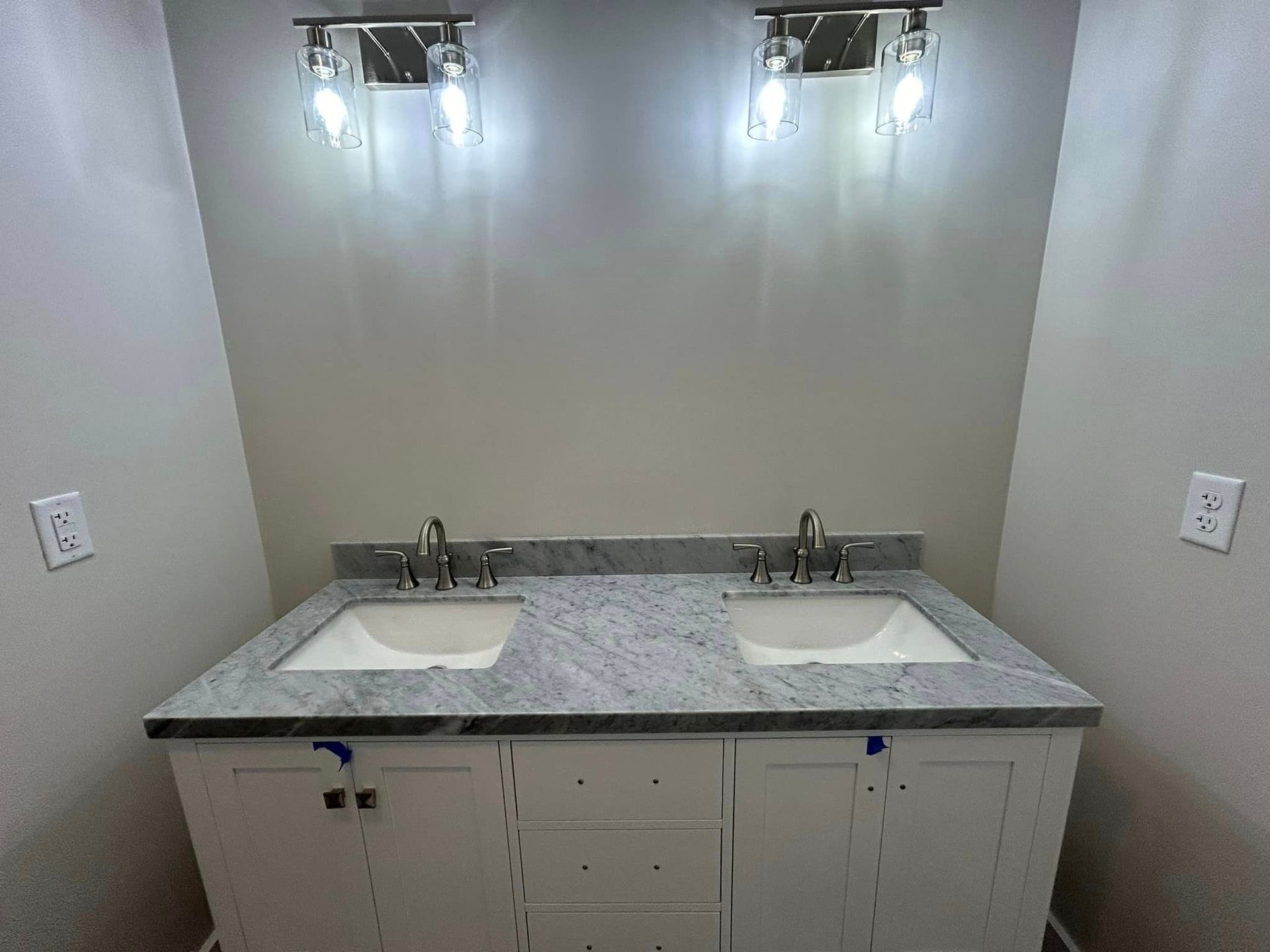 A bathroom with two sinks and two lights on the wall.