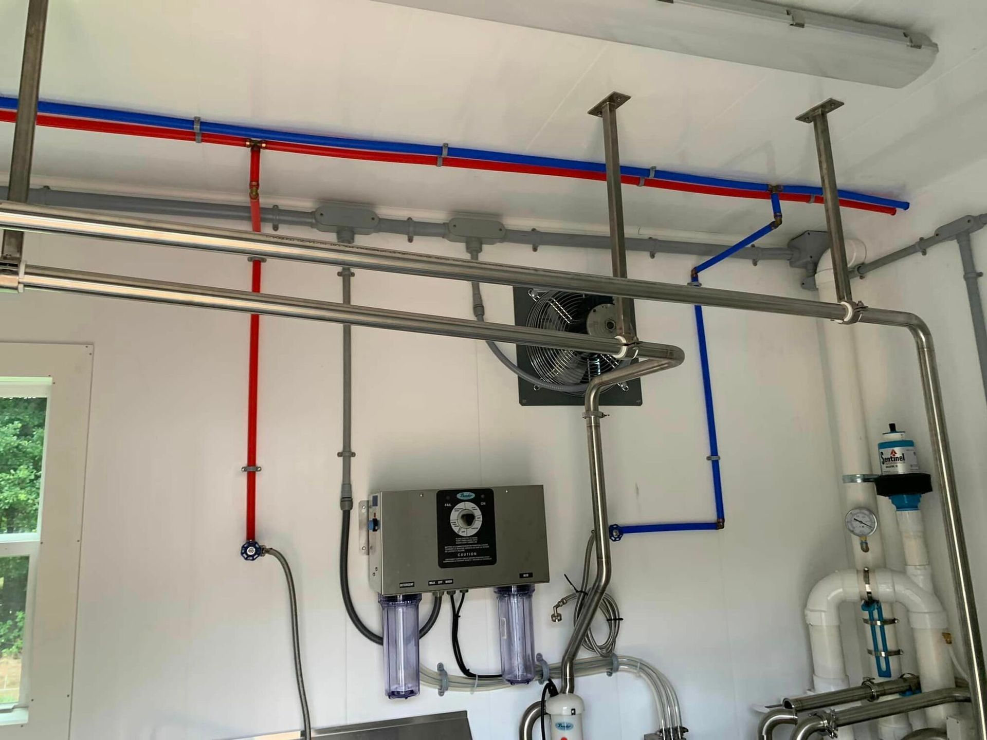 A room with a lot of pipes and a fan on the ceiling.