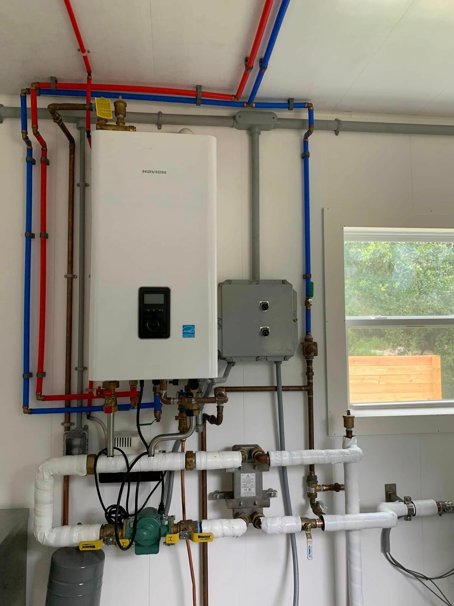 A white water heater is surrounded by red and blue pipes