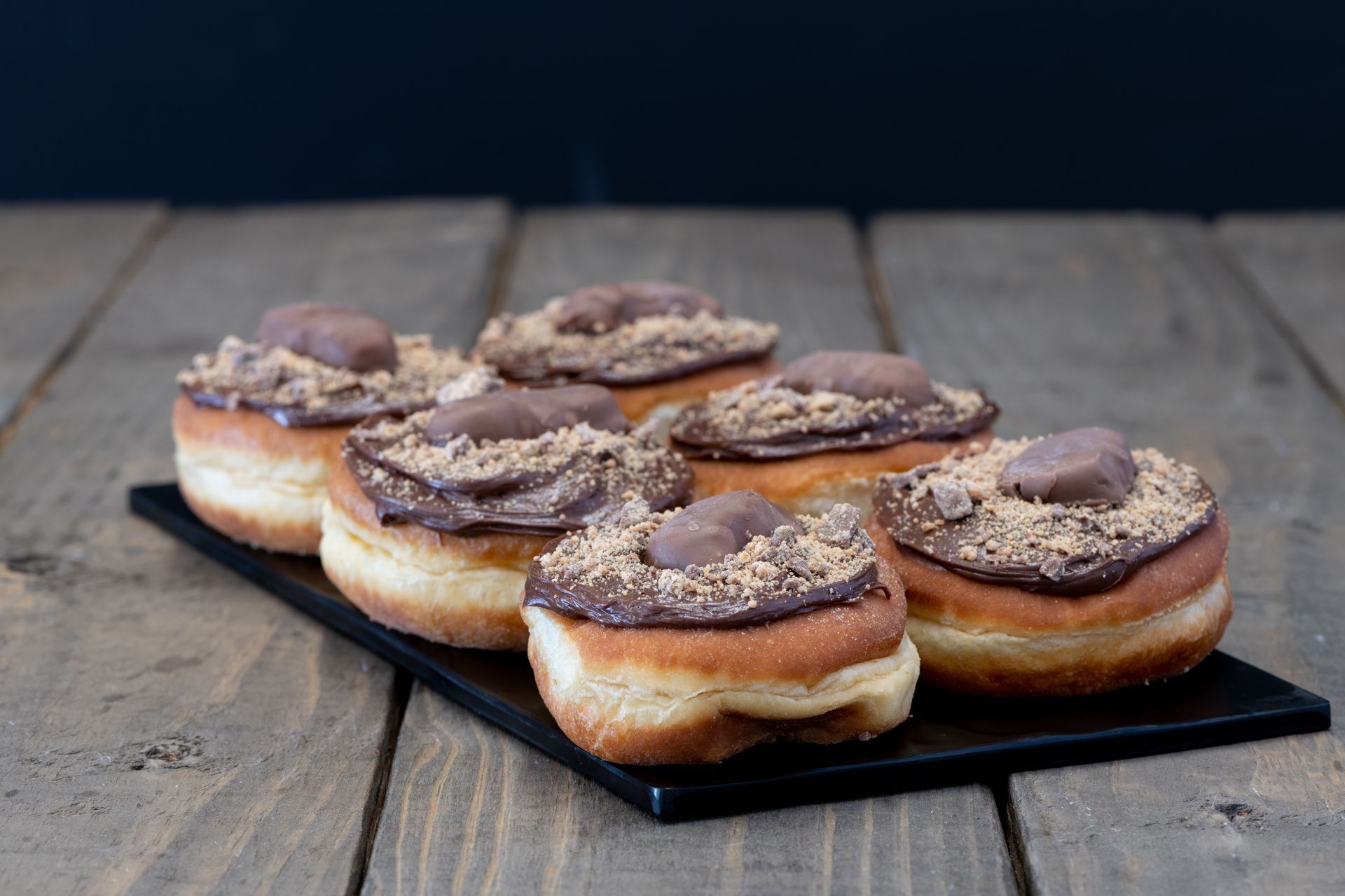 A tray of donuts with chocolate frosting on a wooden table.