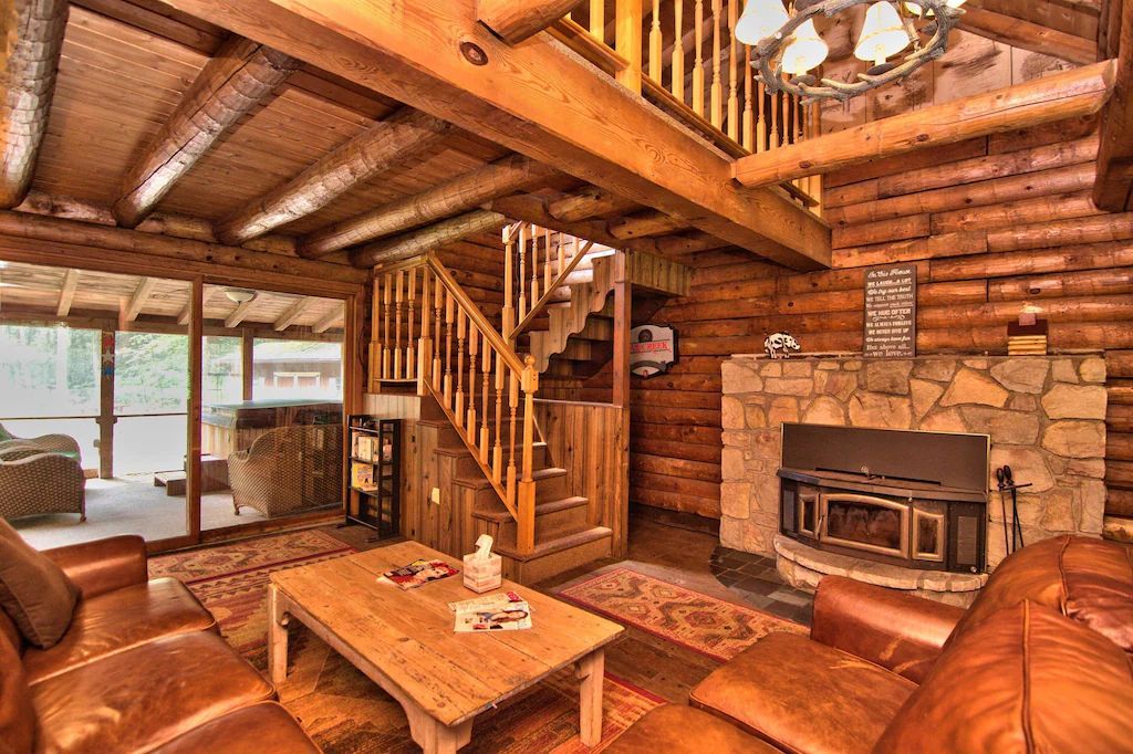 A living room in a log cabin with a fireplace and stairs.