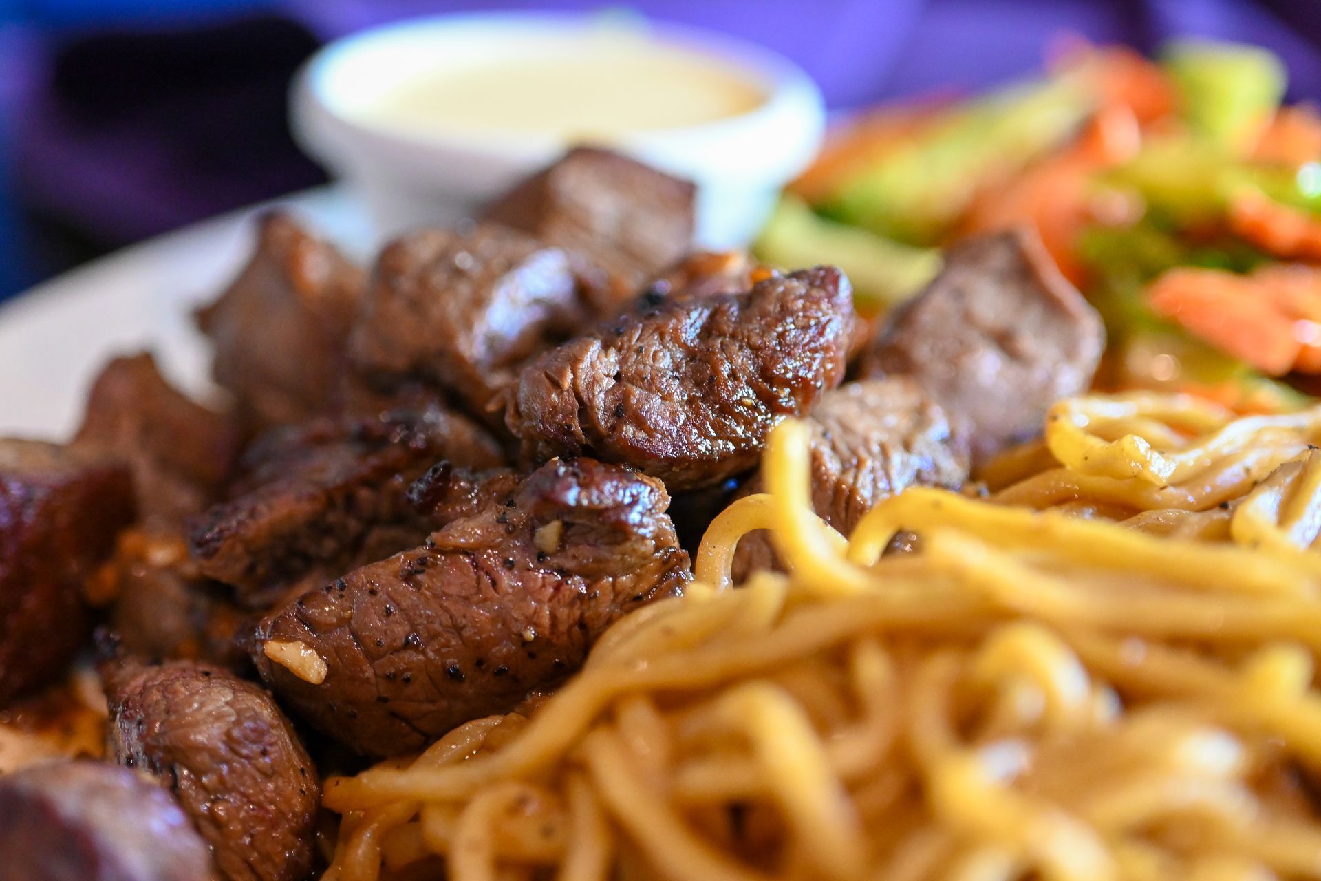 A close up of a plate of food with noodles and meat on a table.