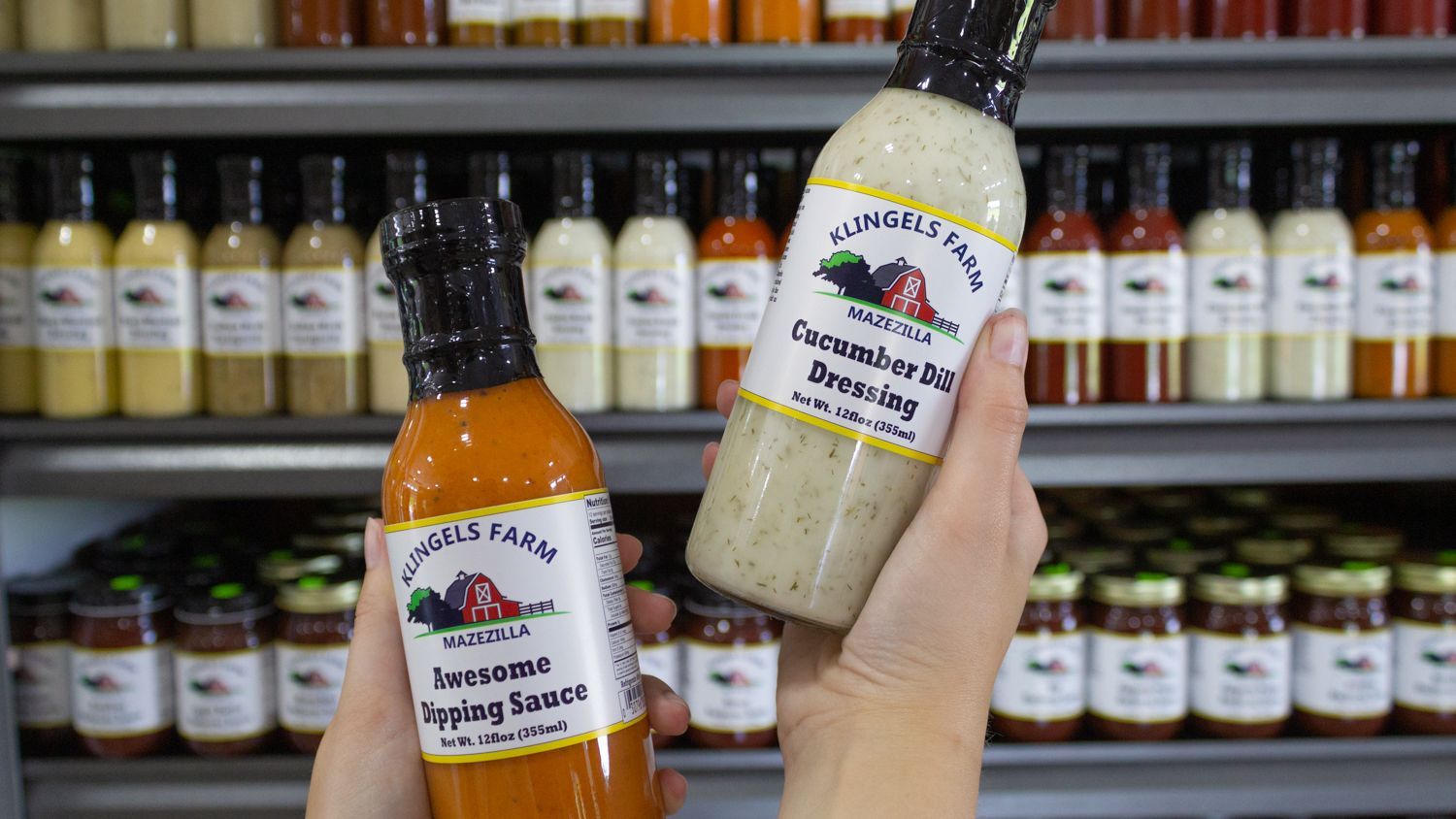 A person is holding two bottles of salad dressing in front of a shelf.