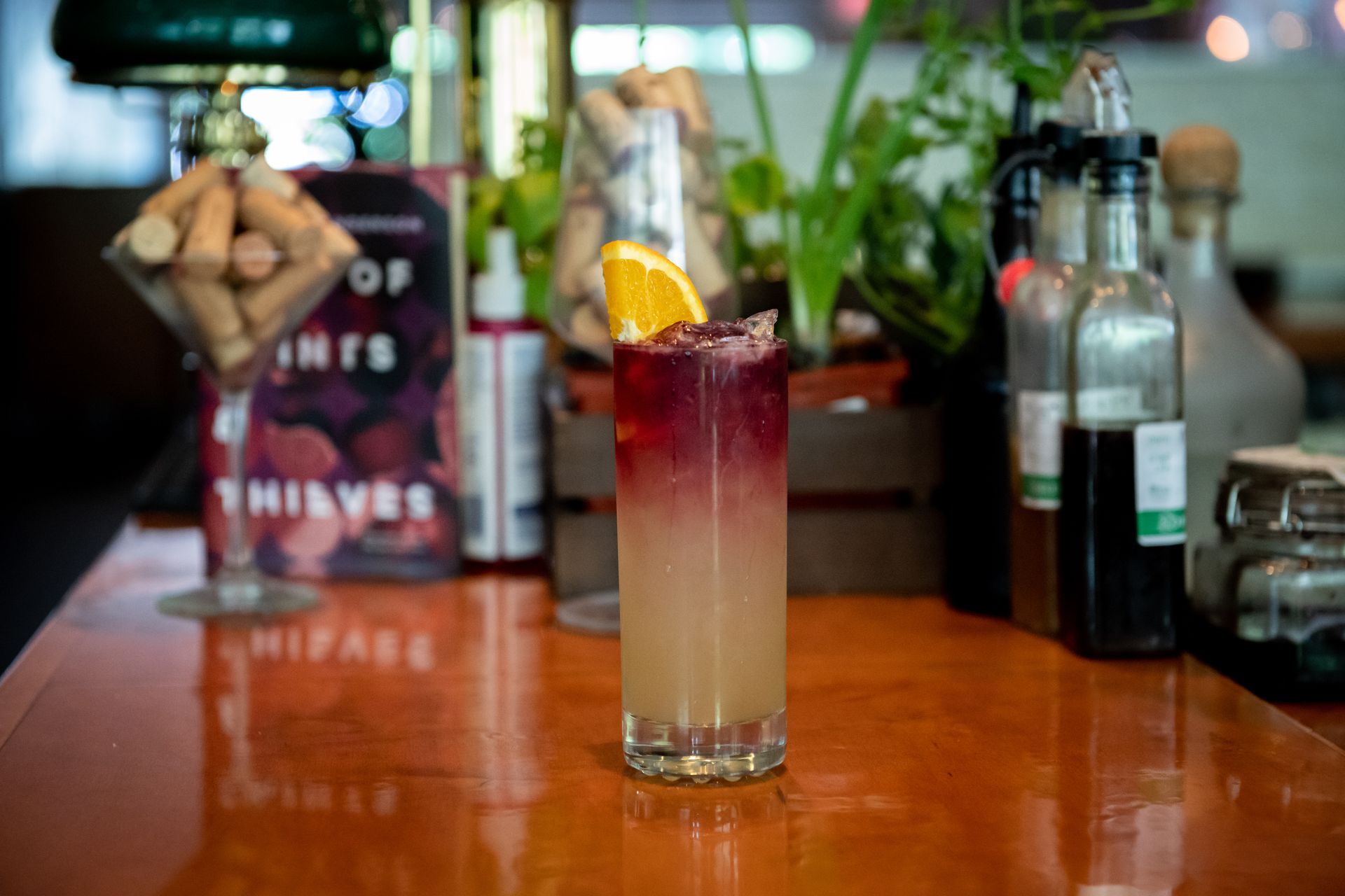 A tall glass filled with a drink is sitting on a wooden bar.