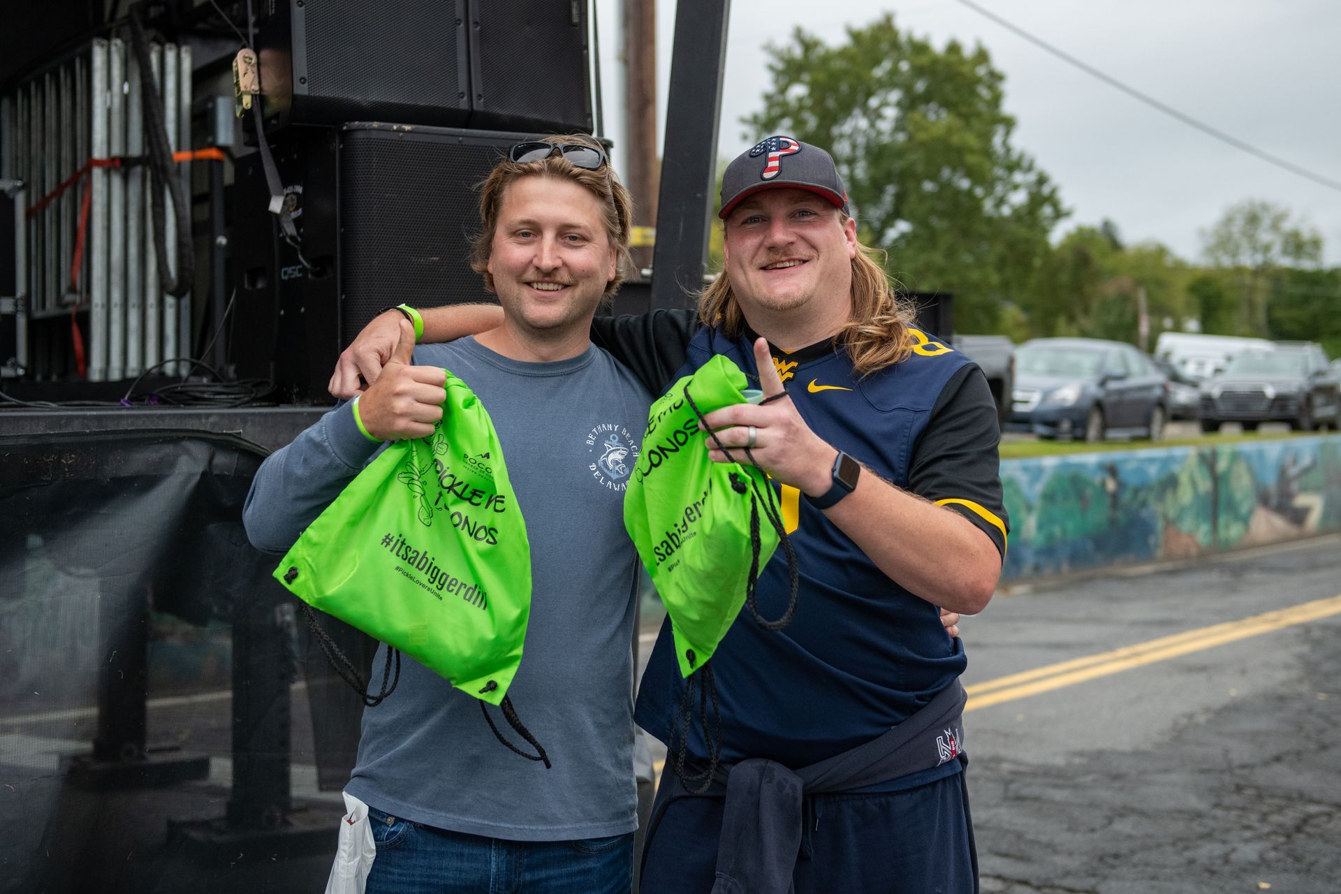 Two men are standing next to each other holding green bags.
