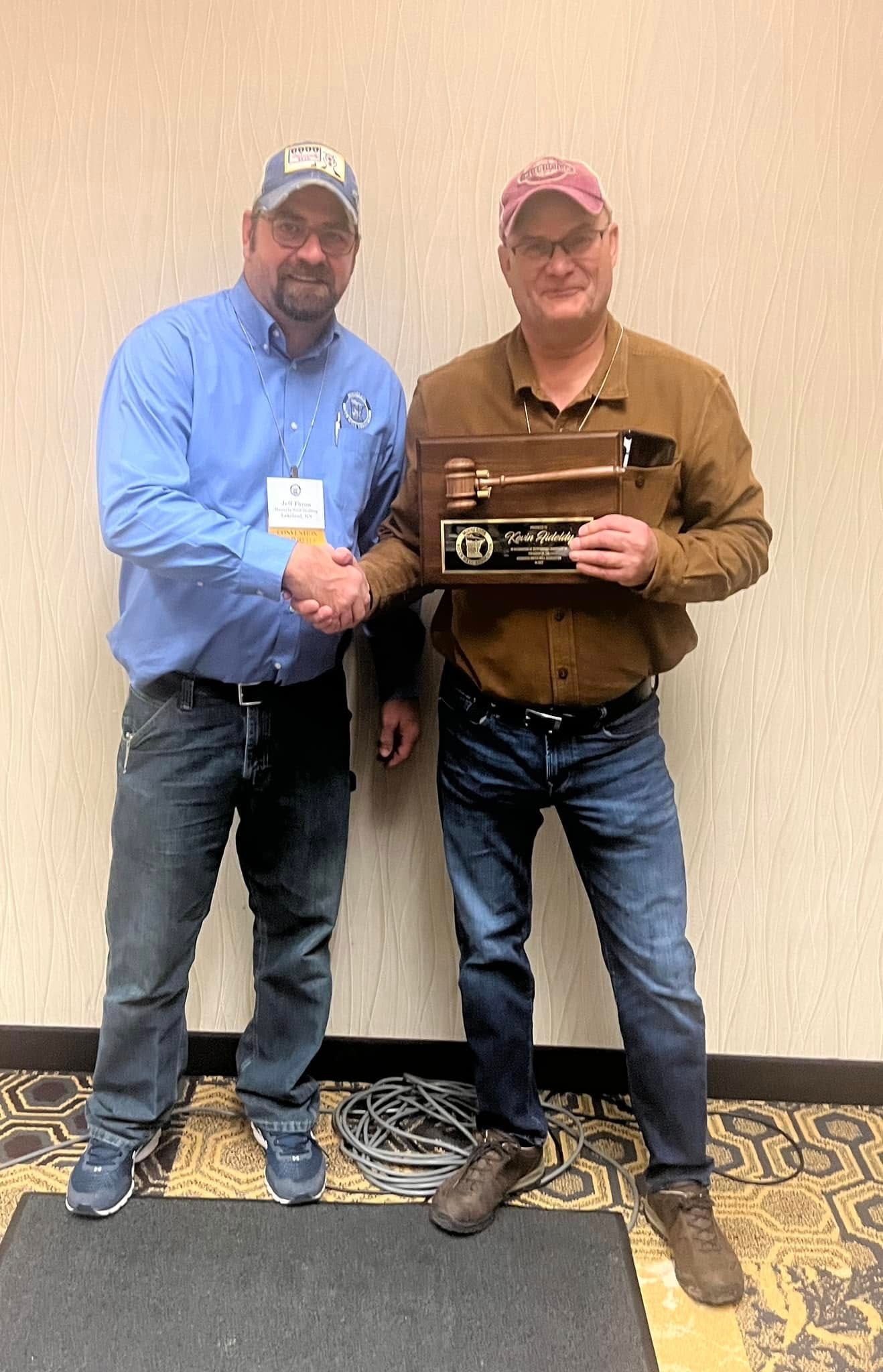Two men are shaking hands while holding a plaque.
