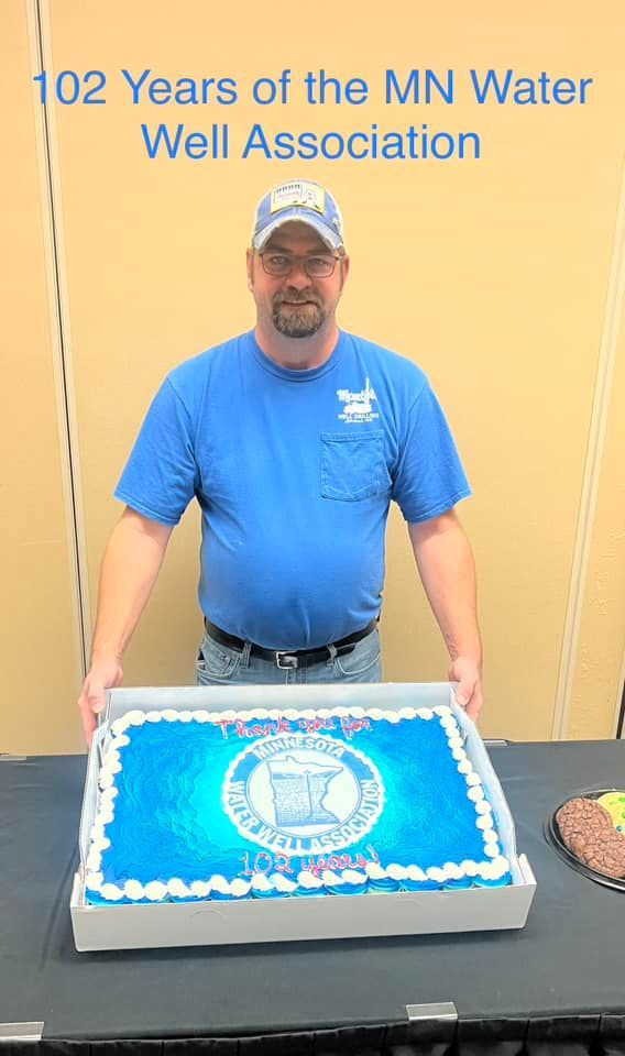 A man in a blue shirt is holding a cake on a table.