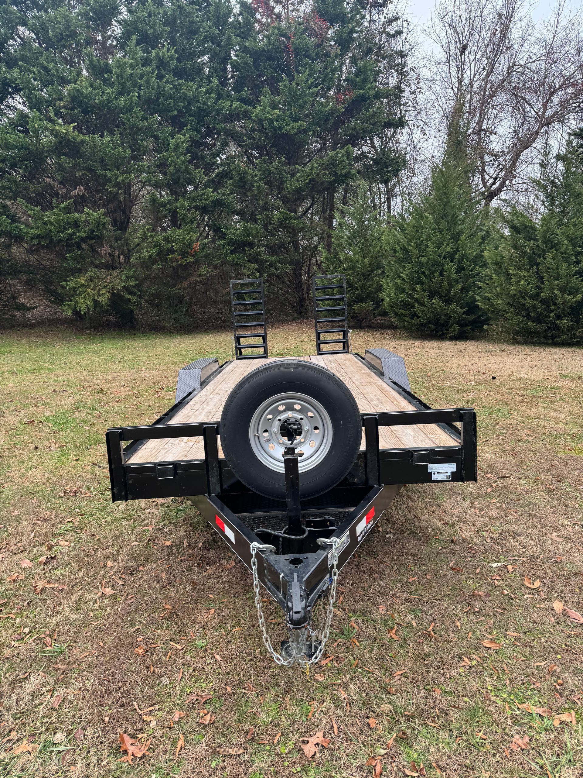 A trailer with a spare tire attached to it is parked in a grassy field.