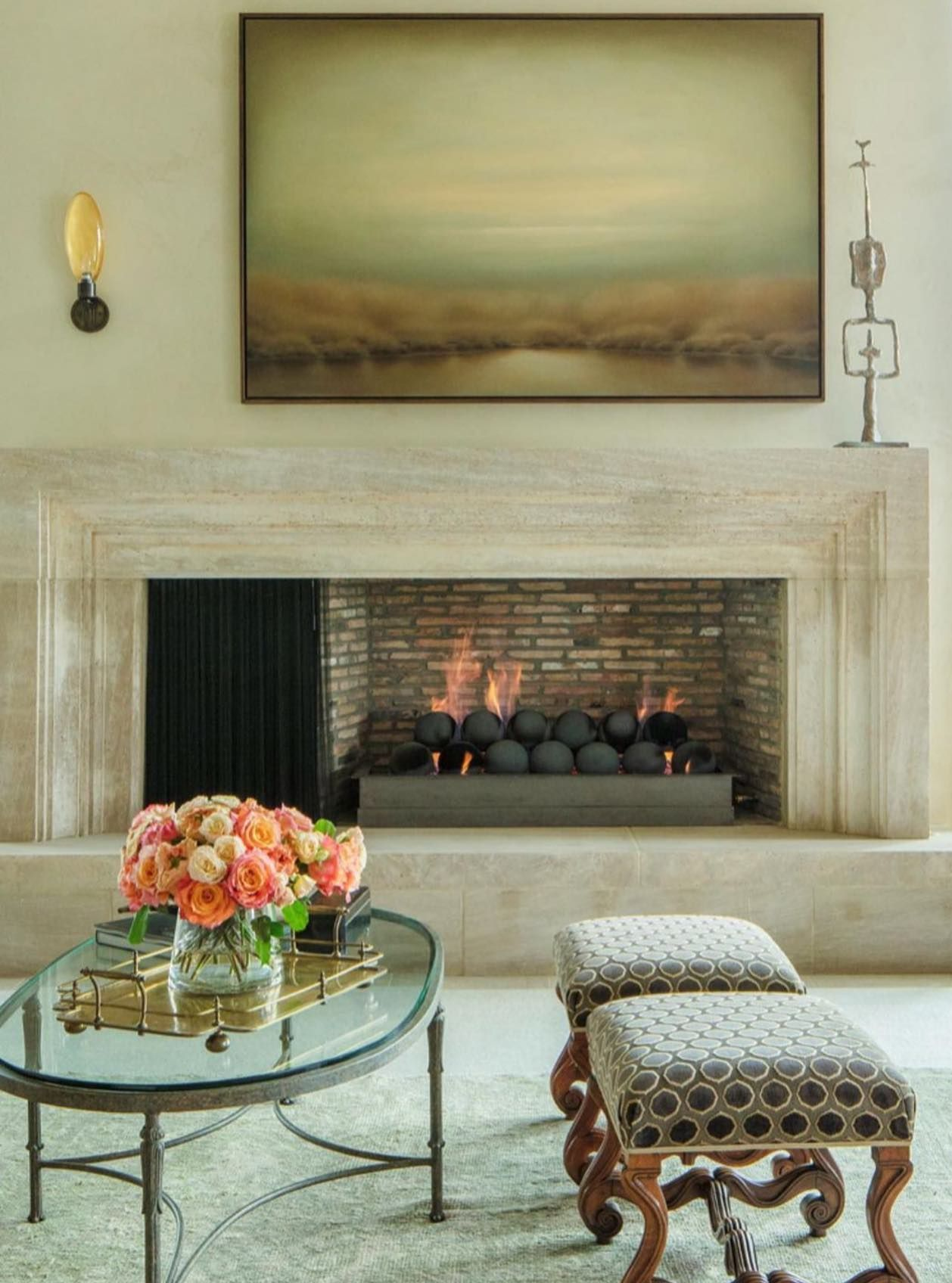 Fireplace with art above, coffee table with flowers, and patterned ottoman seating.