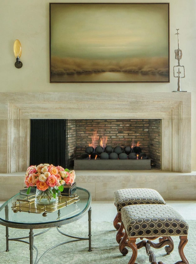 Fireplace with art above, coffee table with flowers, and patterned ottoman seating.