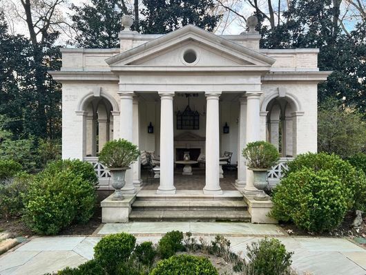 Stone pavilion with columns, front steps, and potted plants in a garden setting.