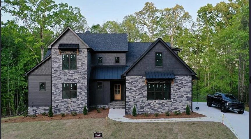 Modern two-story house with gray stone and siding, black roof and trim, parked black truck on driveway.