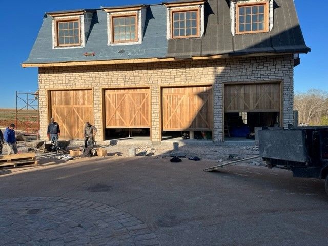 Exterior of a stone building with three garage doors, some open. People stand nearby.
