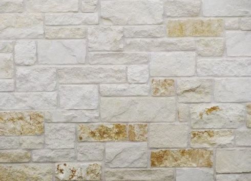 Stone wall with off-white and tan rectangular blocks arranged in a random pattern.