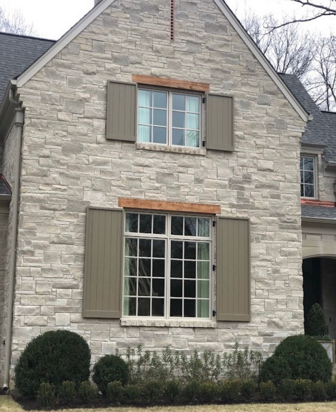 Stone house with olive-green shutters, light-colored windows, and landscaping.