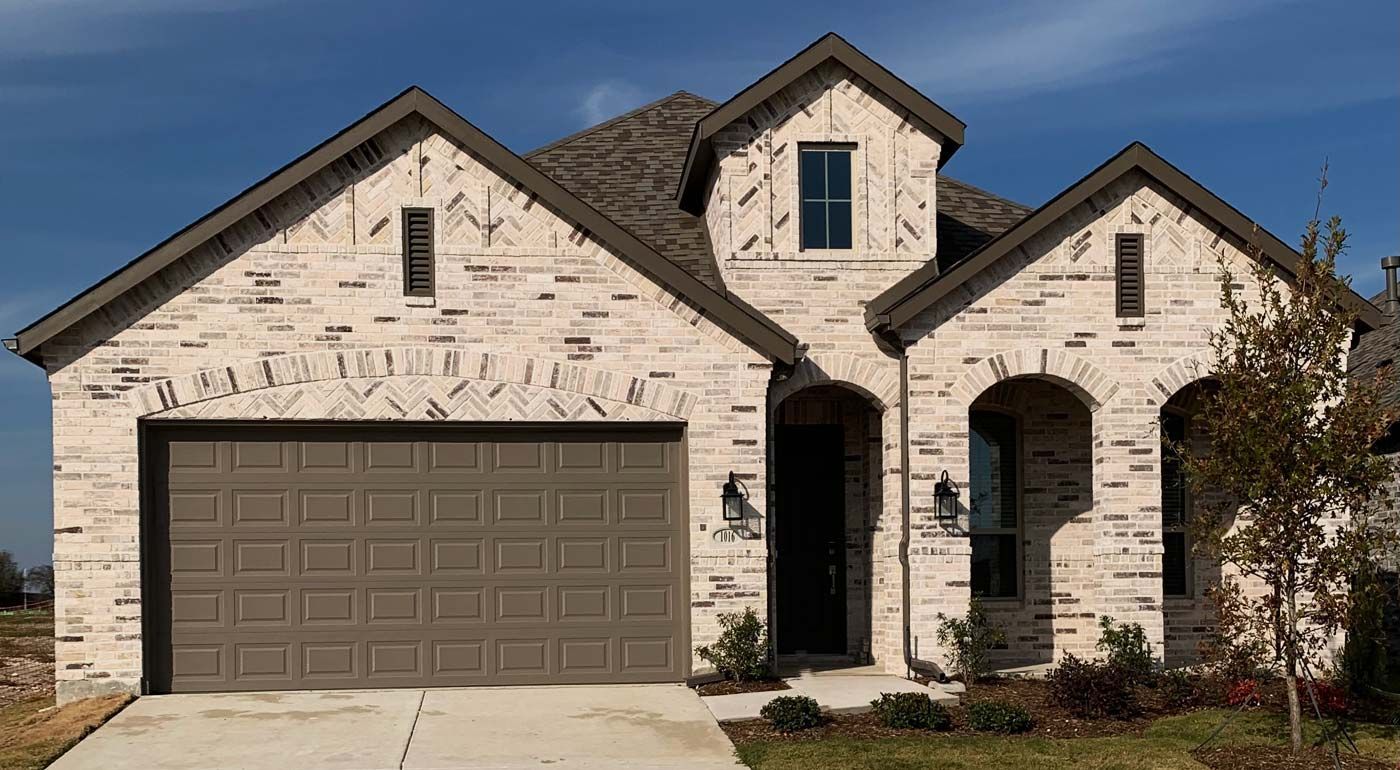 Brick house with brown roof, garage door, and trim against a blue sky.