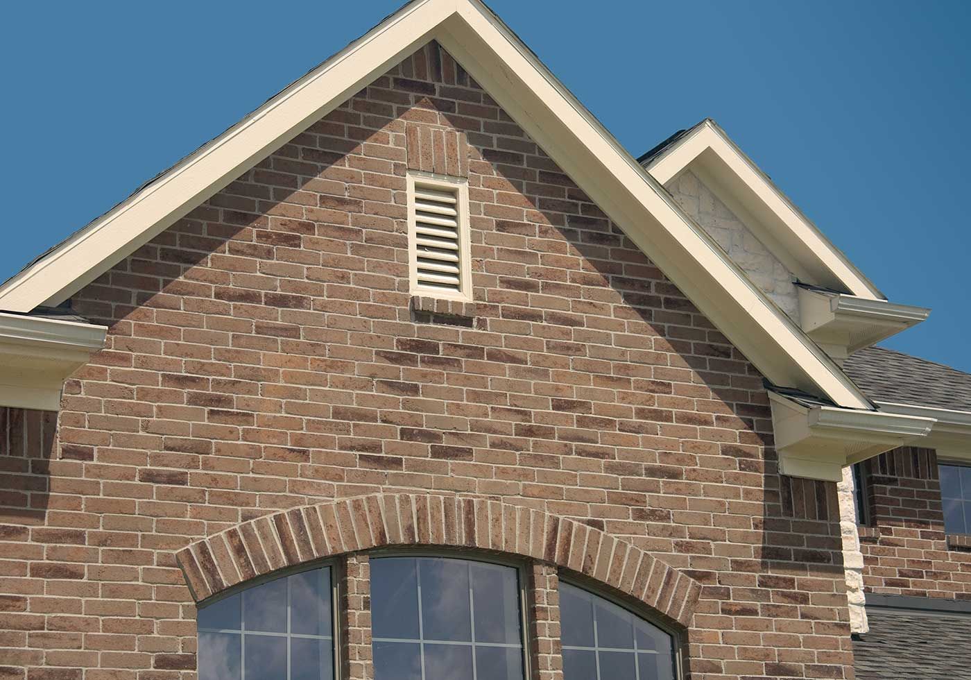 Brick home exterior with arched window, vent, and beige trim.