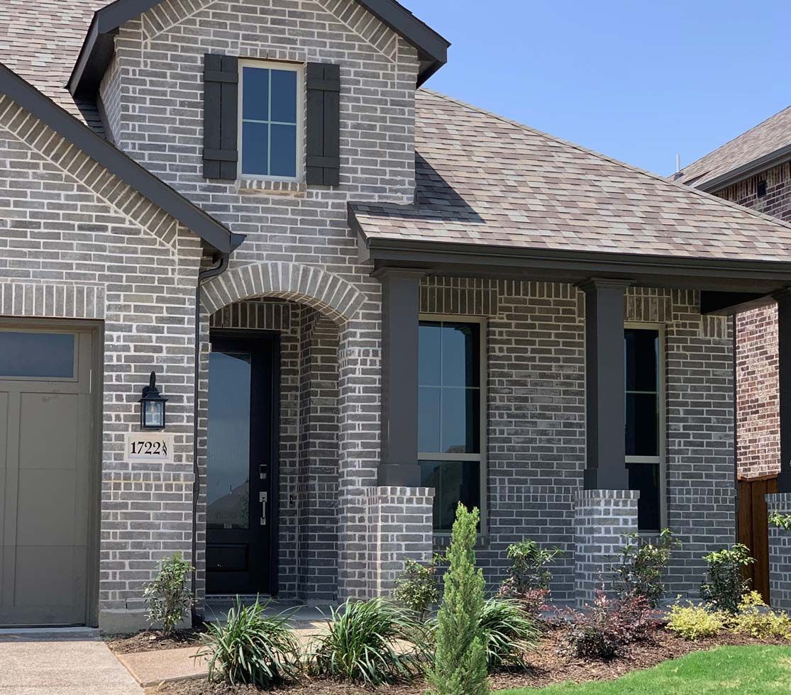 Gray brick house with dark gray trim, black door, and landscaping under a blue sky.