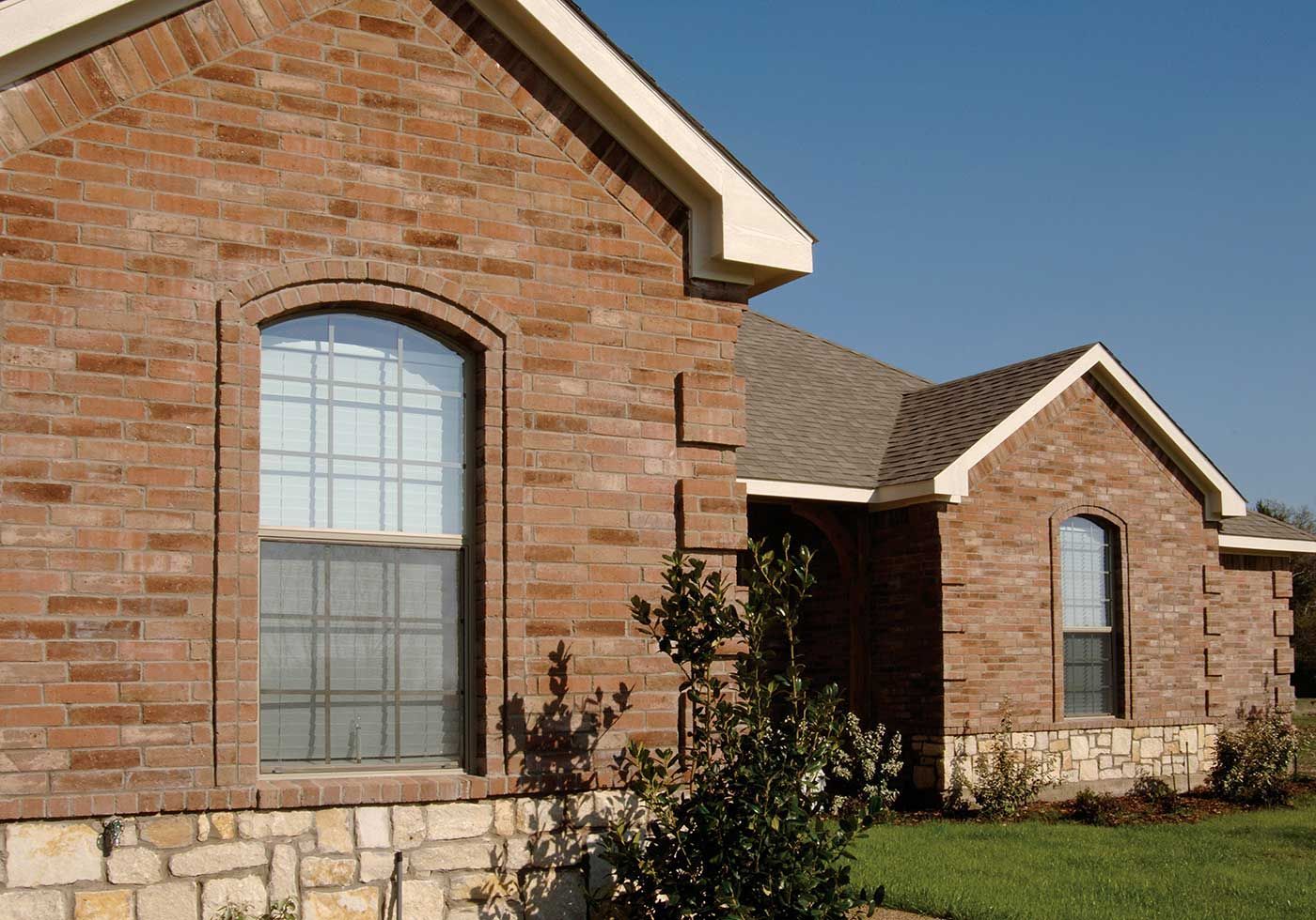 Brick house with arched windows and stone foundation under a blue sky.