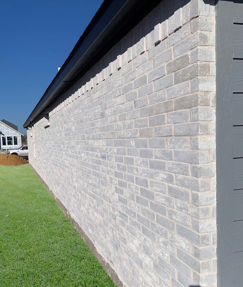 Brick exterior wall of a building, painted light gray, with a dark roof against a clear blue sky.