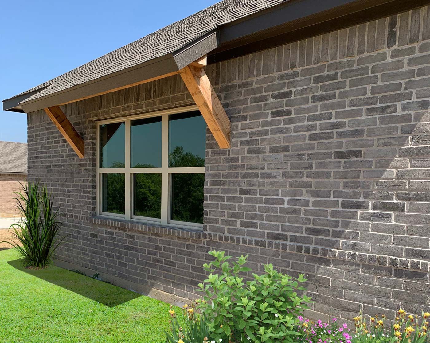 Brick exterior of a house with a window, wooden supports, and landscaping under a sunny sky.